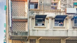 A multi-story building with patterned exterior walls, a ground-level entrance, and a row of parked motorcycles. - Hotel Decent (Surat)