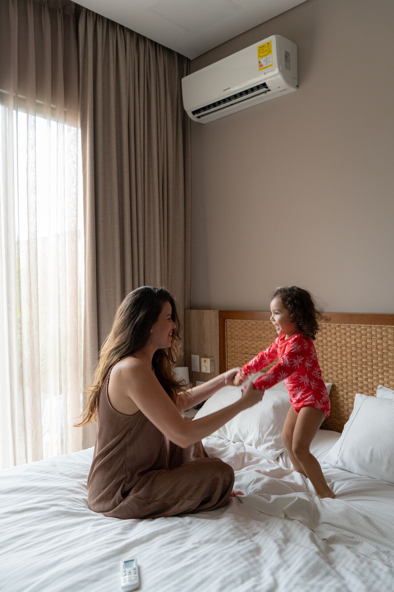 Habitación de hotel con cama, aire acondicionado de pared y ventana con cortinas.