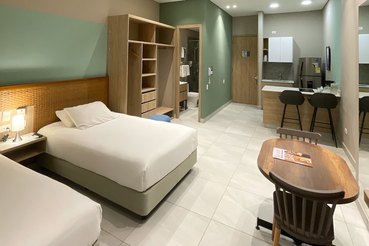 A hotel room with a bed, a desk, a chair, a wardrobe, and a bathroom visible through an open door.
