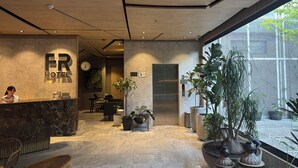 A hotel reception area with a marble floor, a reception desk, a clock, and a large window with plants. - FR Hotel (Ibagué)