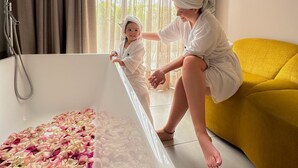 A bathtub filled with rose petals, a yellow sofa, and a window with curtains. - FR Hotel (Ibagué)