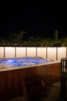 A hot tub with a wooden surround, a bench, and a wall with plants.