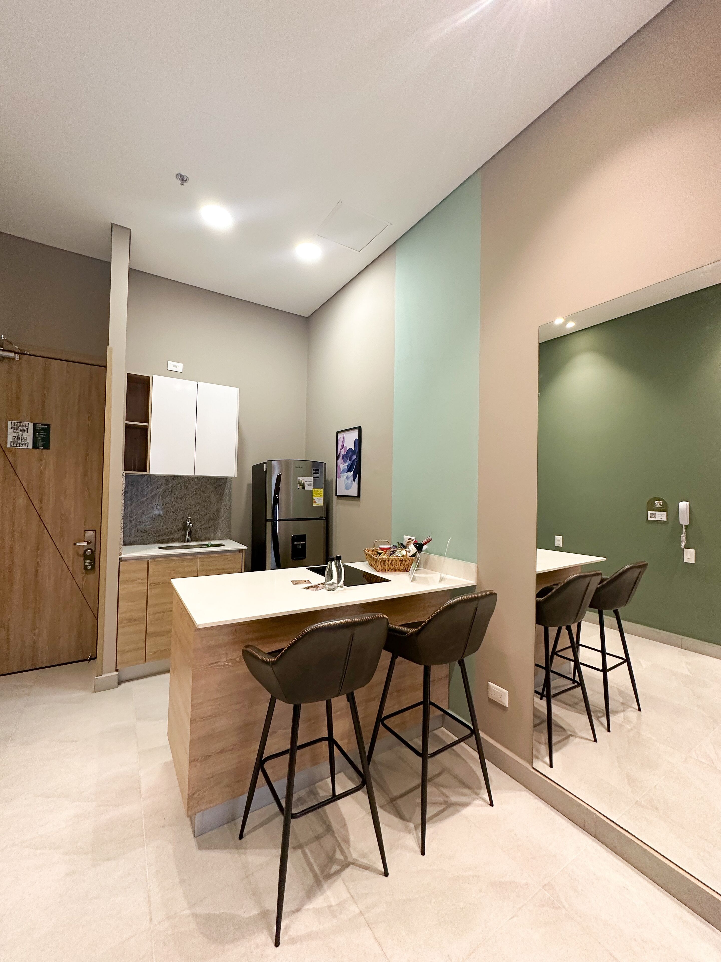 Uma cozinha moderna com uma ilha central, banquetas, geladeira e porta de madeira.