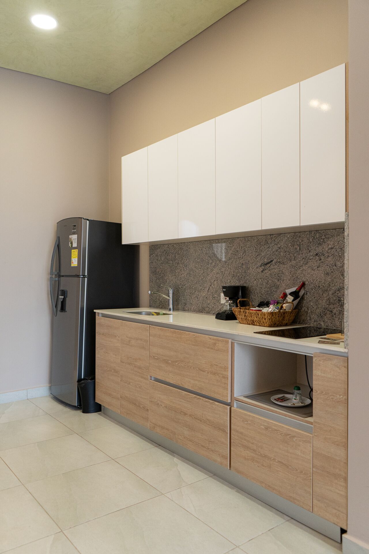 A modern kitchen with a built-in refrigerator, wooden cabinets, a granite countertop, and a basket of items on the counter.