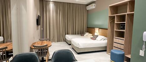 Una habitación de hotel moderna con zona de comedor, dos camas, televisor y armario.