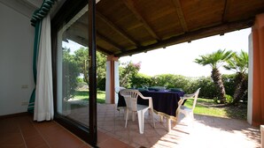 A covered patio with a table set for dining, a sliding glass door leading to a garden, and a wooden ceiling. - Villa Camilla private garden and pool. 30% DISCOUNT, PERIOD 24 MAY - 7 JUNE (Punta de Su Turrione Stintino ( SS))