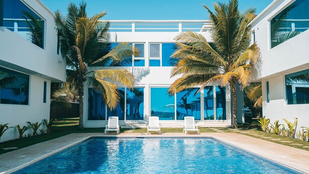 Een zwembad in moderne stijl met helderblauw water, witte ligbedden en palmbomen.