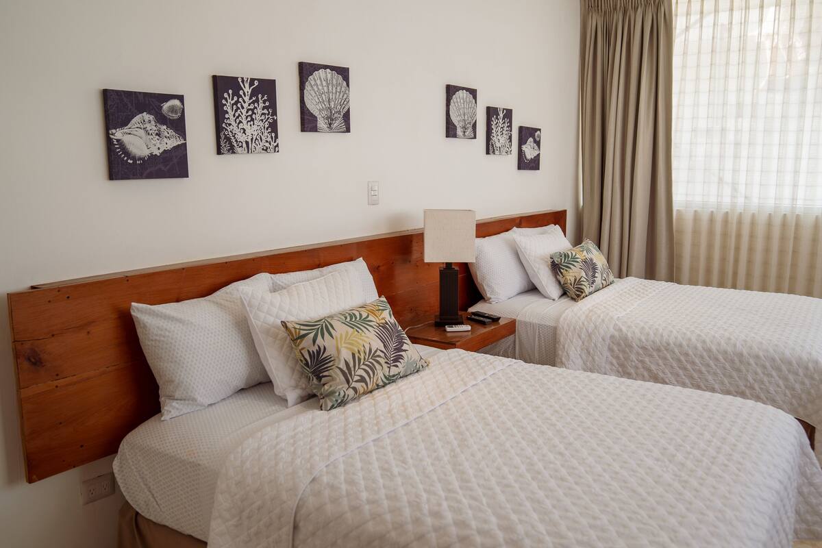 Een hotelkamer met twee bedden, een nachtkastje met een lamp en decoratie aan de muur.