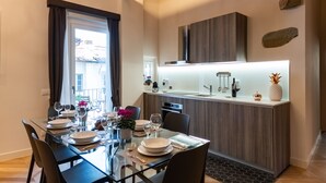 Un comedor moderno con una mesa de vidrio, sillas oscuras y una isla de cocina con un lavabo y objetos decorativos.