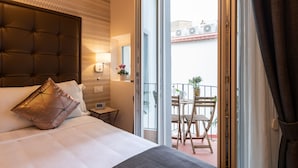 Habitación de hotel con una cama grande, una mesita de noche, una lámpara y vistas a un balcón con mesa y sillas.