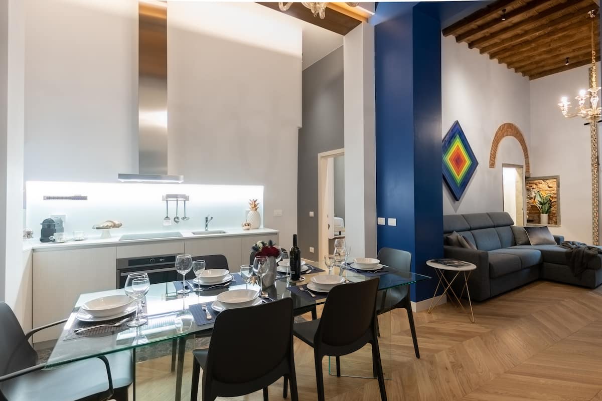 Una sala moderna con una mesa de comedor de cristal, sofás oscuros y una pared de acento azul.