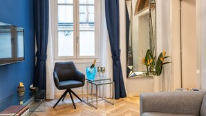 Una sala moderna con un sillón de cuero negro, una mesa de centro de vidrio y un sofá gris. También se ve un espejo grande y una planta en maceta.