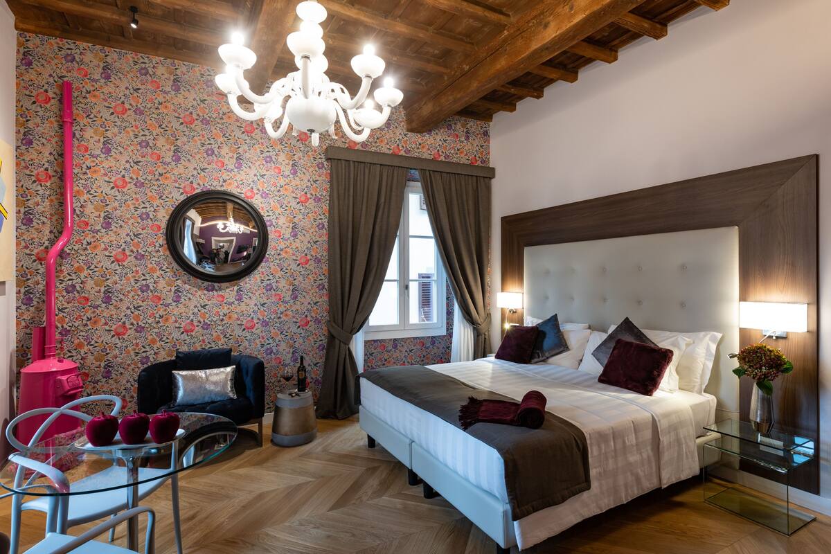 Un dormitorio con una cama grande, una araña, un espejo y papel tapiz con motivos florales.