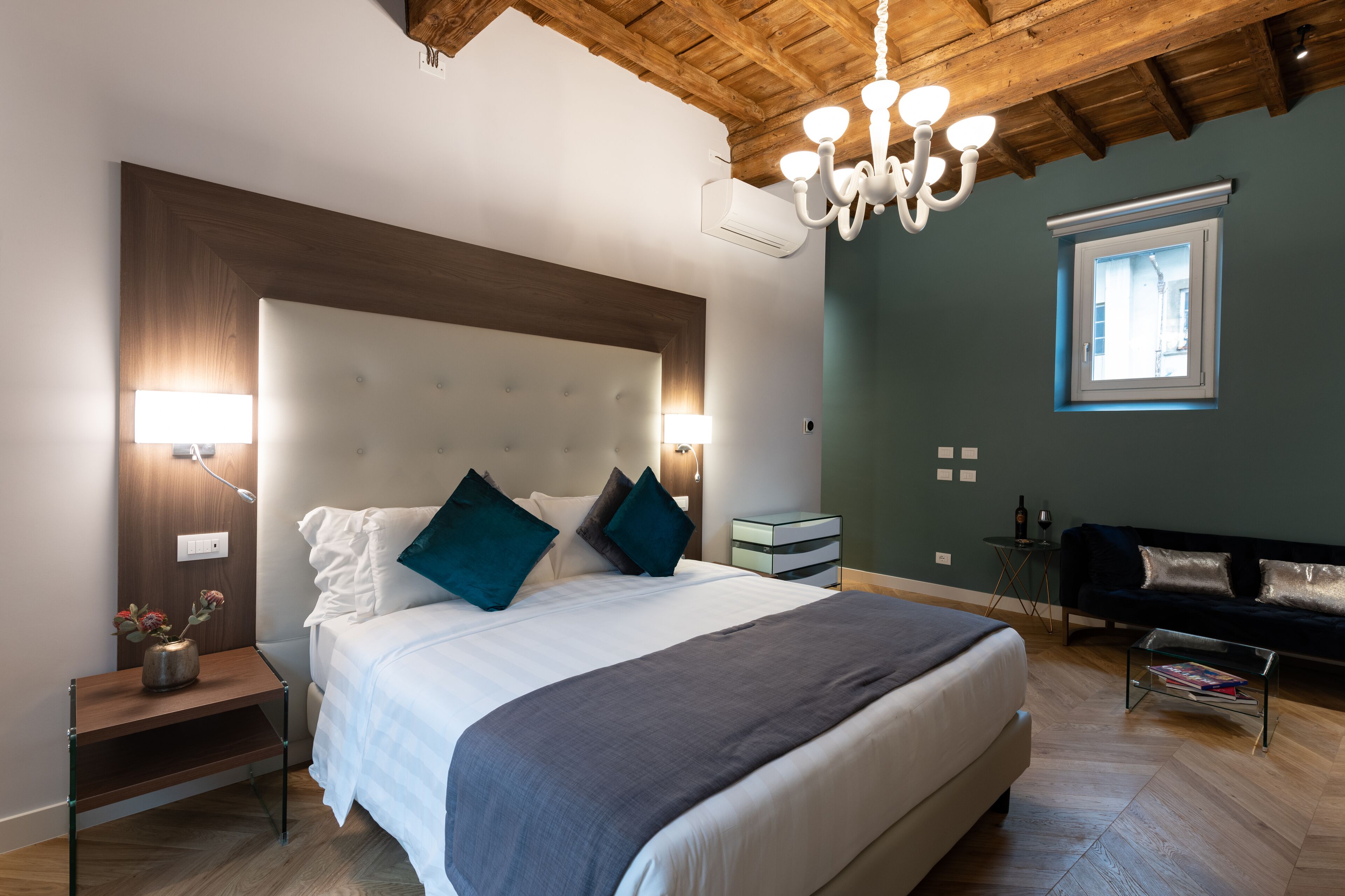 Een moderne slaapkamer met een groot bed, nachtlampjes, een klein tafeltje met een vaas, en een raam met uitzicht.