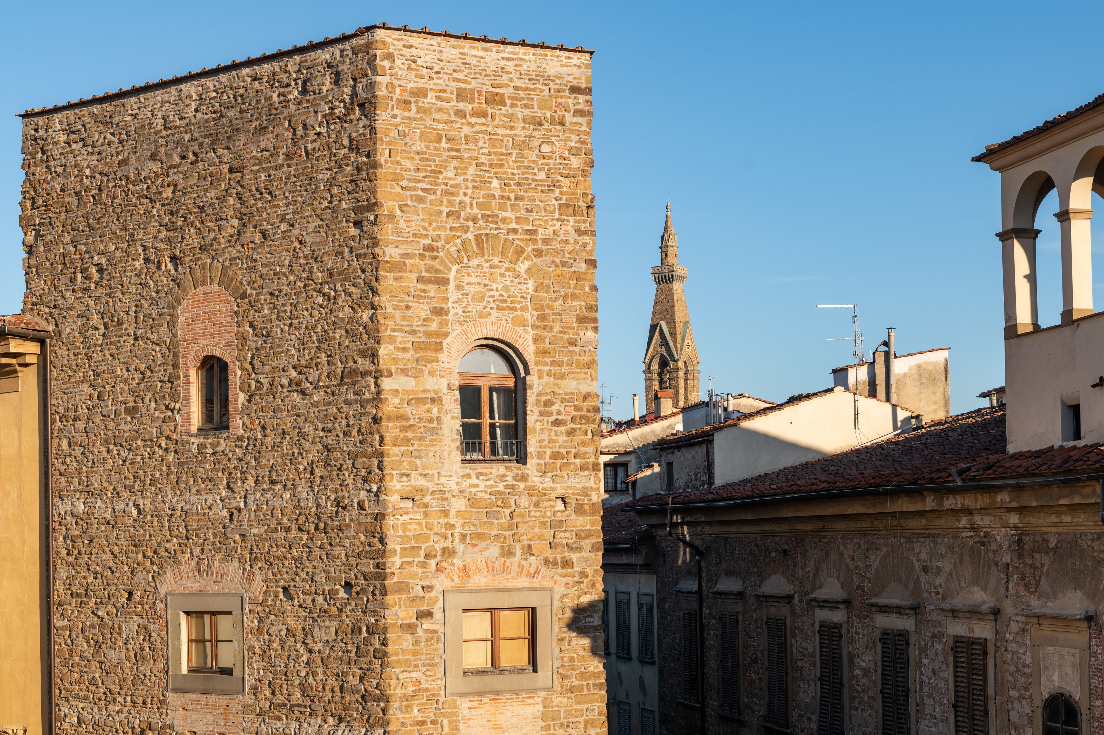 A stone building with arched windows and a tower in the background.