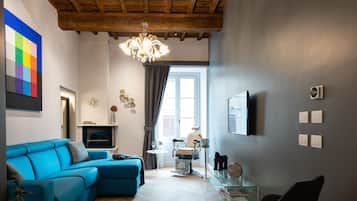 Una sala de estar moderna con un sofá seccional azul, una mesa de centro de vidrio, una silla negra y un piso de madera con patrón de espiga.