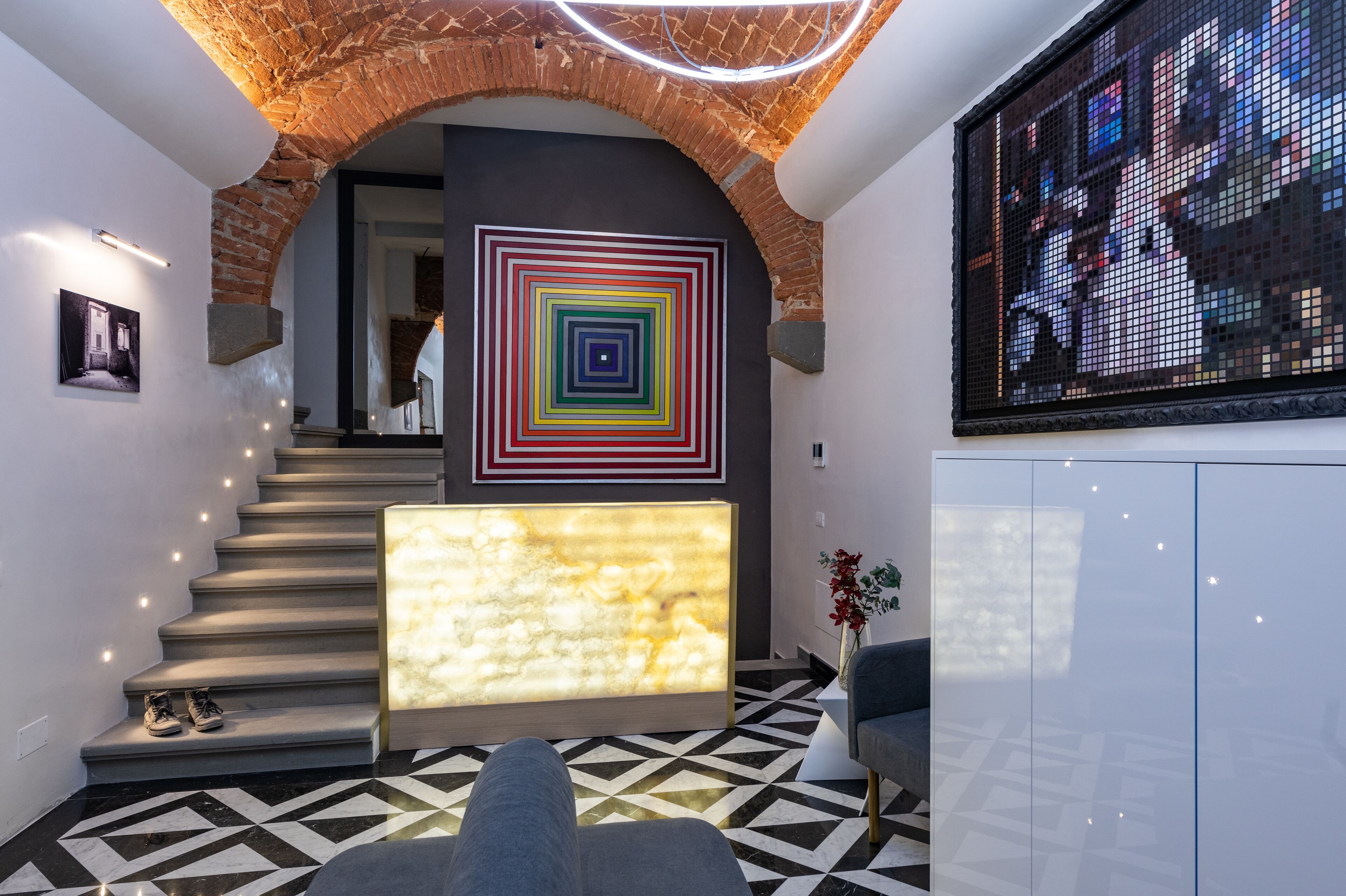 A modern interior with a staircase, a colorful geometric wall art, and a digital display.