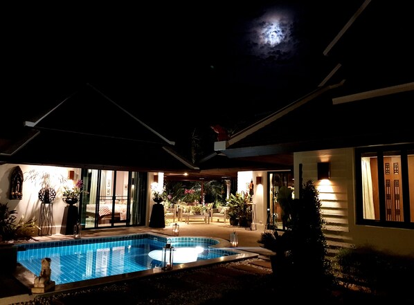 Ein Nachtblick auf einen Poolbereich mit klarem Himmel, Mond und einem Gebäude mit großen Fenstern und Außenbereich.