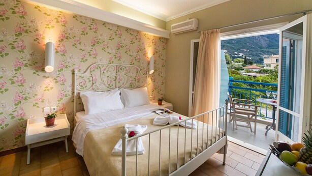 A hotel room with a bed, bedside table, and a balcony with a table and chairs. - Sunny Garden (Lefkada)