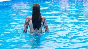 A swimming pool with a person in the water, surrounded by lounge chairs and greenery. - Sunny Garden (Lefkada)