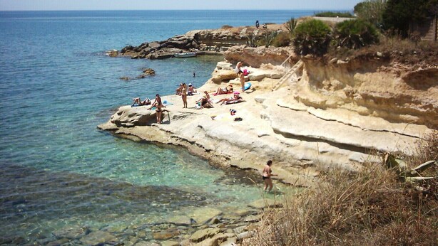 A rocky coastal area with clear water, people sunbathing, and a boat in the distance. - Villa Lucia 50 meters from the sea (Avola)
