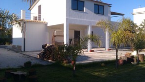 A two-story white building with a flat roof and large windows. There are several potted plants and a small outdoor seating area. - Villa Lucia 50 meters from the sea (Avola)
