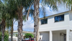 A modern two-story house with a patio area, surrounded by palm trees and potted plants. - Villa Lucia 50 meters from the sea (Avola)
