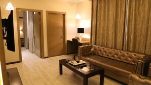 Ein modernes Hotelzimmer mit Ledersofa, Glastisch, Flachbildfernseher und großem Fenster mit Vorhängen.