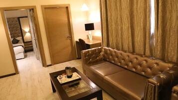 A hotel room with a brown leather sofa, a wooden coffee table with a tray of items, a lamp on a side table, and a door leading to a bathroom.