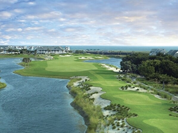 Un parcours de golf avec un plan d’eau, des arbres et un bâtiment situé au loin.