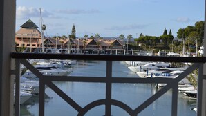 Marina com barcos atracados, um edifício com telhado em formato de pirâmide e palmeiras ao fundo.