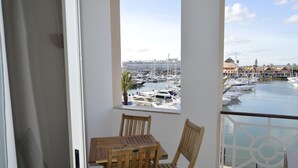 Varanda com mesa e cadeiras de madeira, vista para uma marina com barcos e edifícios.