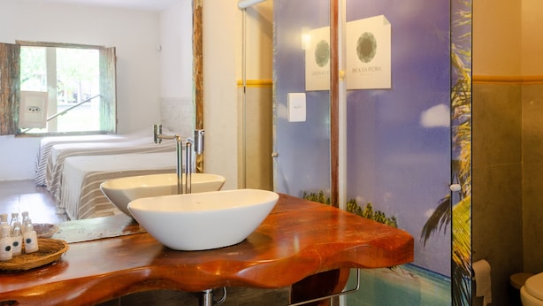 A bathroom with a large mirror, a white sink, and a wooden vanity. There are two beds visible in the background. - Pousada Bica Da Pedra (Marechal Deodoro)