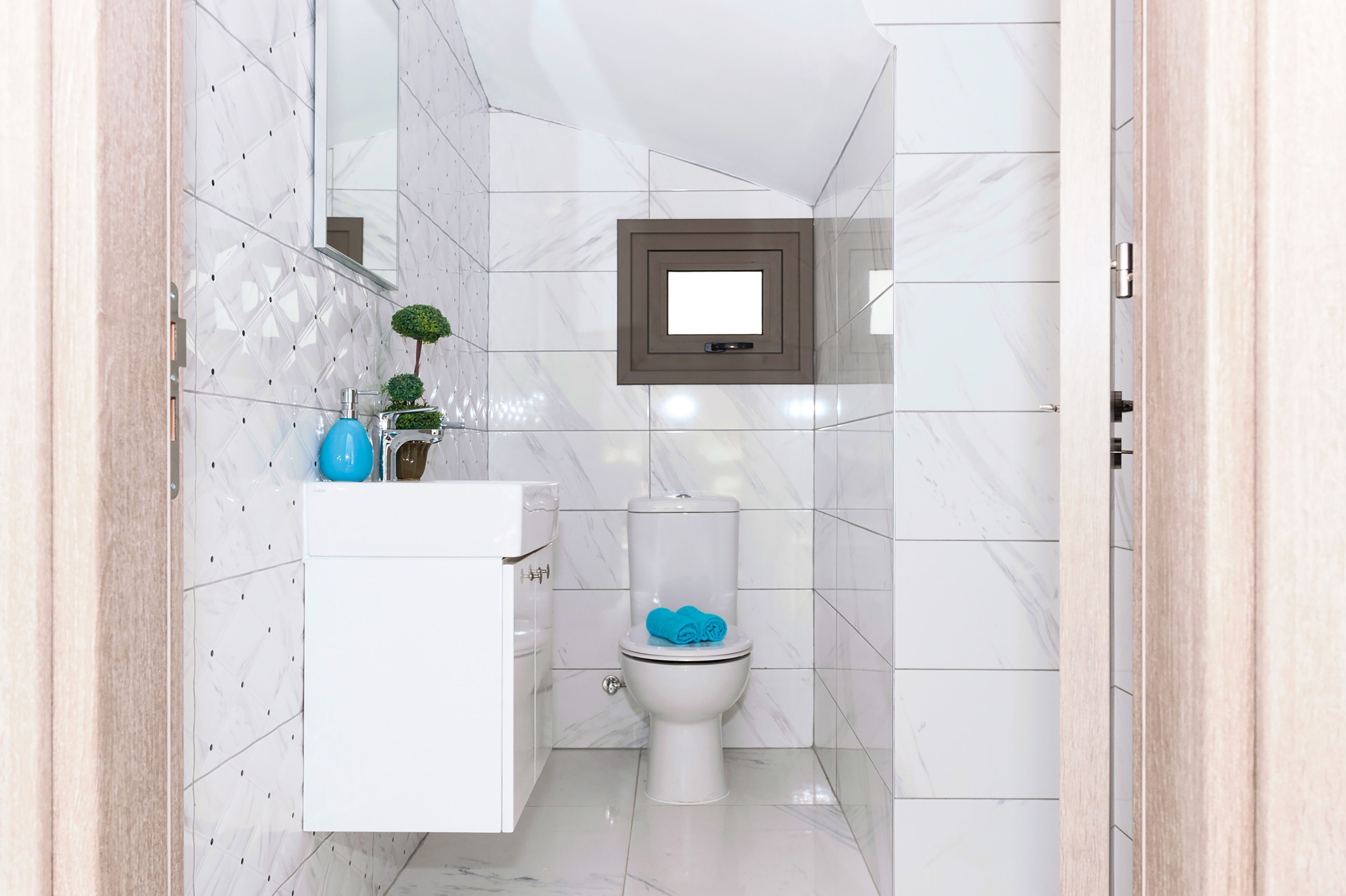 A bathroom with white marble tiles, a white toilet, a small mirror, and a blue vase on the sink.