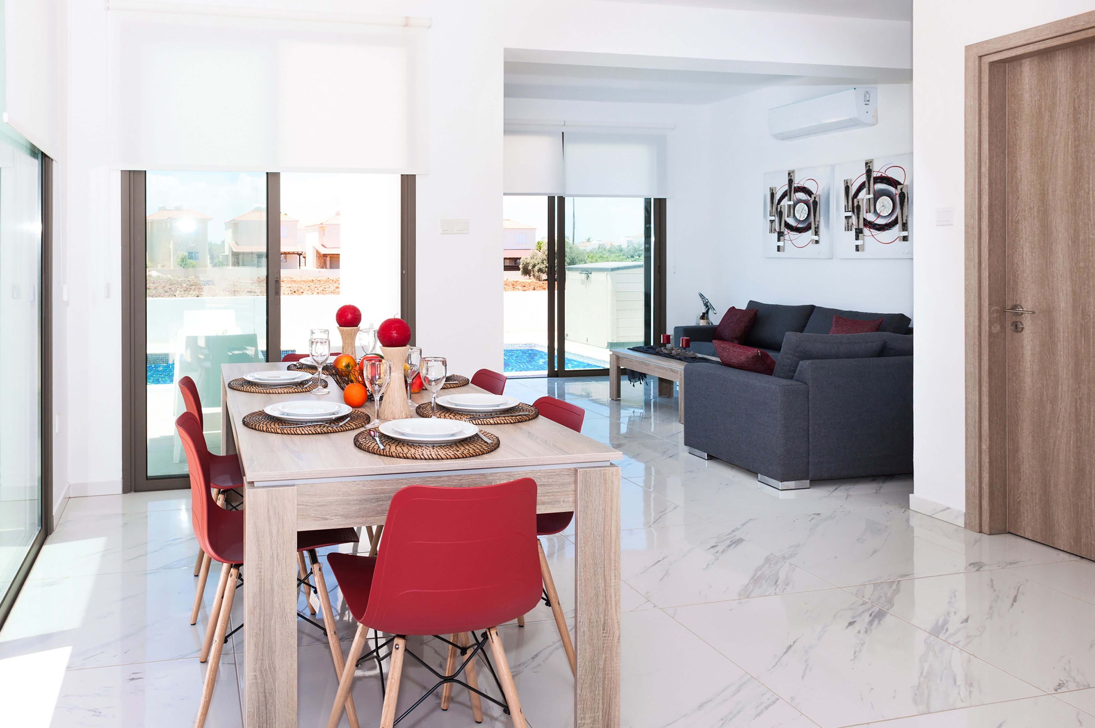 Un comedor moderno con una mesa grande, sillas rojas y vistas a una piscina.