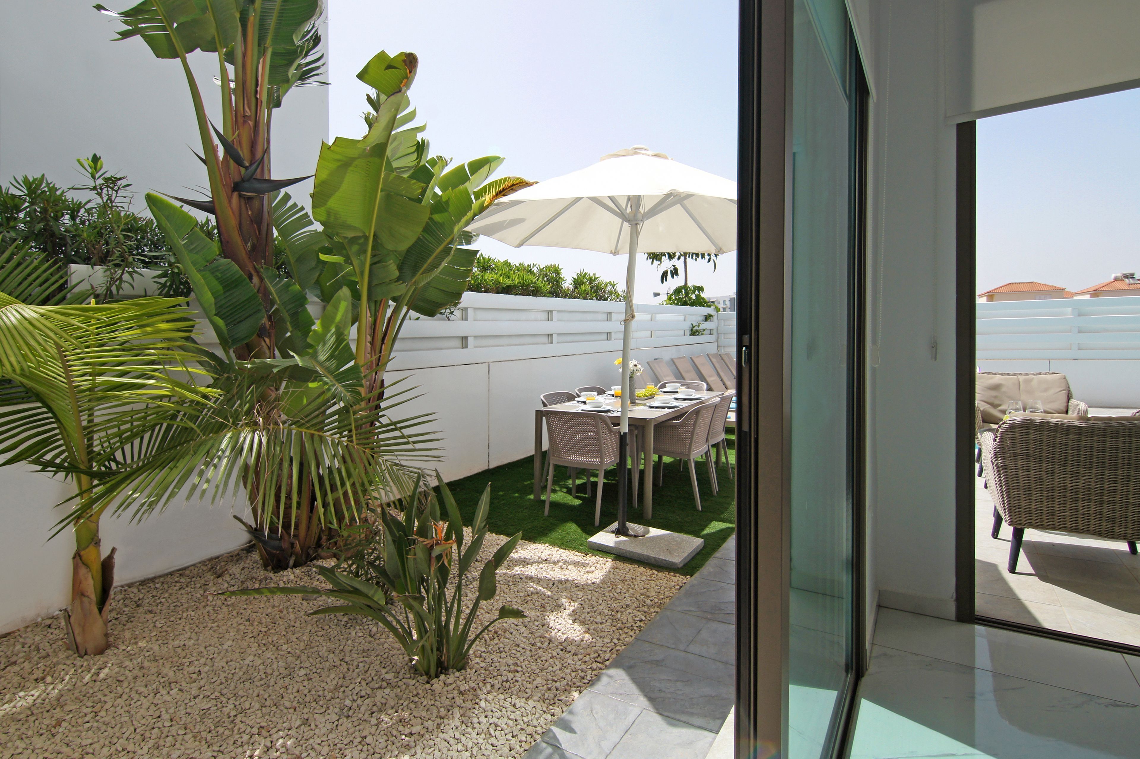 Un patio con mesa y sillas, rodeado de plantas y una valla blanca.