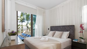 A modern hotel room with a large bed, a glass desk, and a view of palm trees through the window. - SERENA - Brand New 4Bed Villa walking distance to Trinity Golden Sandy Beach (Paralimni)