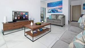 A modern living room with a flat-screen TV, a wooden coffee table, a grey sofa, and a painting on the wall. - SERENA - Brand New 4Bed Villa walking distance to Trinity Golden Sandy Beach (Paralimni)