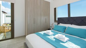 A modern hotel room with a large bed, a balcony with wicker furniture, and a sliding door leading to a balcony. - SERENA - Brand New 4Bed Villa walking distance to Trinity Golden Sandy Beach (Paralimni)