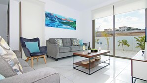 Una sala de estar moderna con un sofá gris, un sillón azul y una mesa de centro con una botella y un vaso.