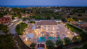 A large building with a swimming pool, outdoor seating, and a view of the sea. - Tramonto Ibleo Resort (Avola)