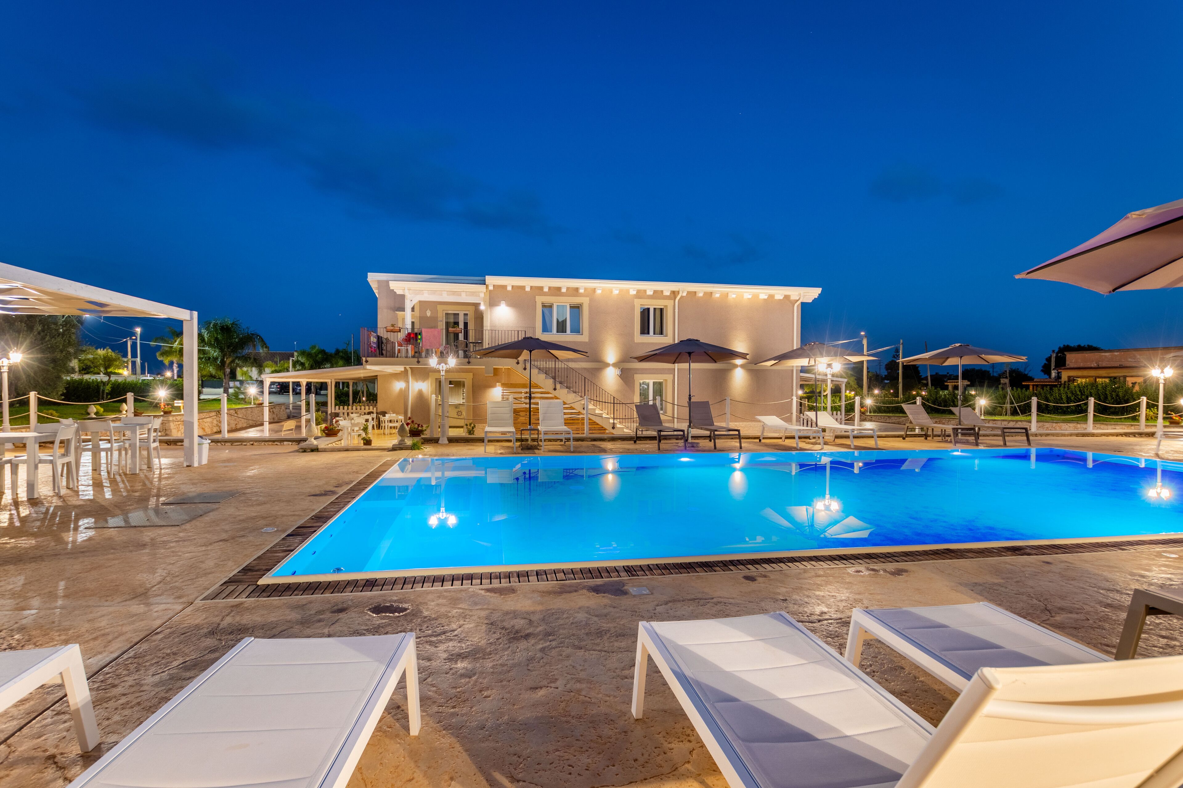 A swimming pool with lounge chairs, a building with multiple windows, and outdoor lighting.