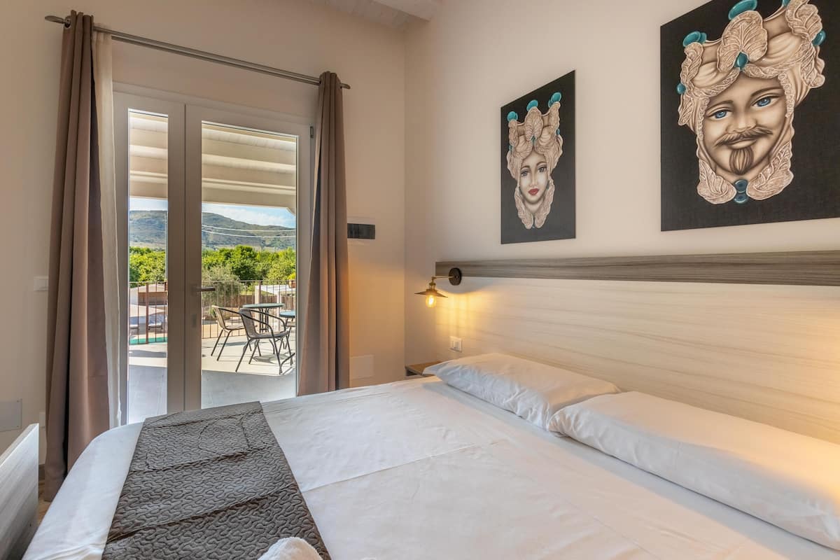 A hotel room with a bed, a view of the outdoors, and artwork on the wall.