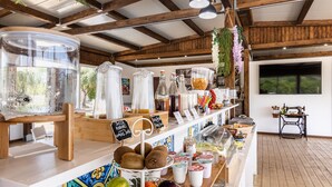 A café with a wooden interior, a counter with various food items, and a view of the outdoors. - Tramonto Ibleo Resort (Avola)