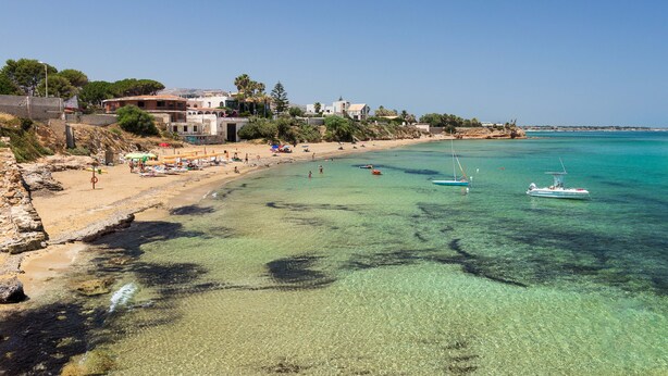 A coastal beach with clear turquoise waters, a sandy shore, and a few boats. - Tramonto Ibleo Resort (Avola)