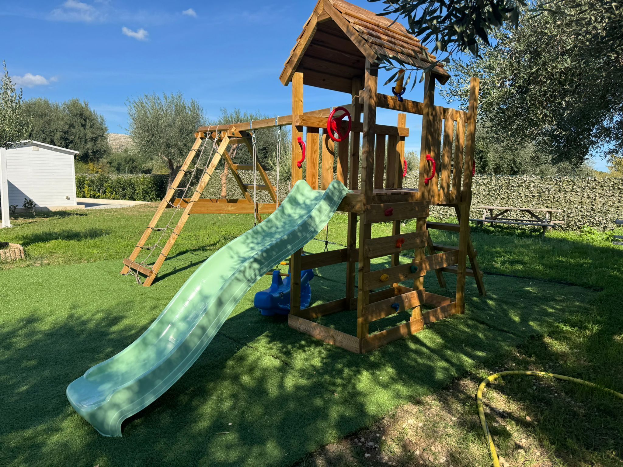 Een houten speelconstructie met een glijbaan en klimmuur in een achtertuin.