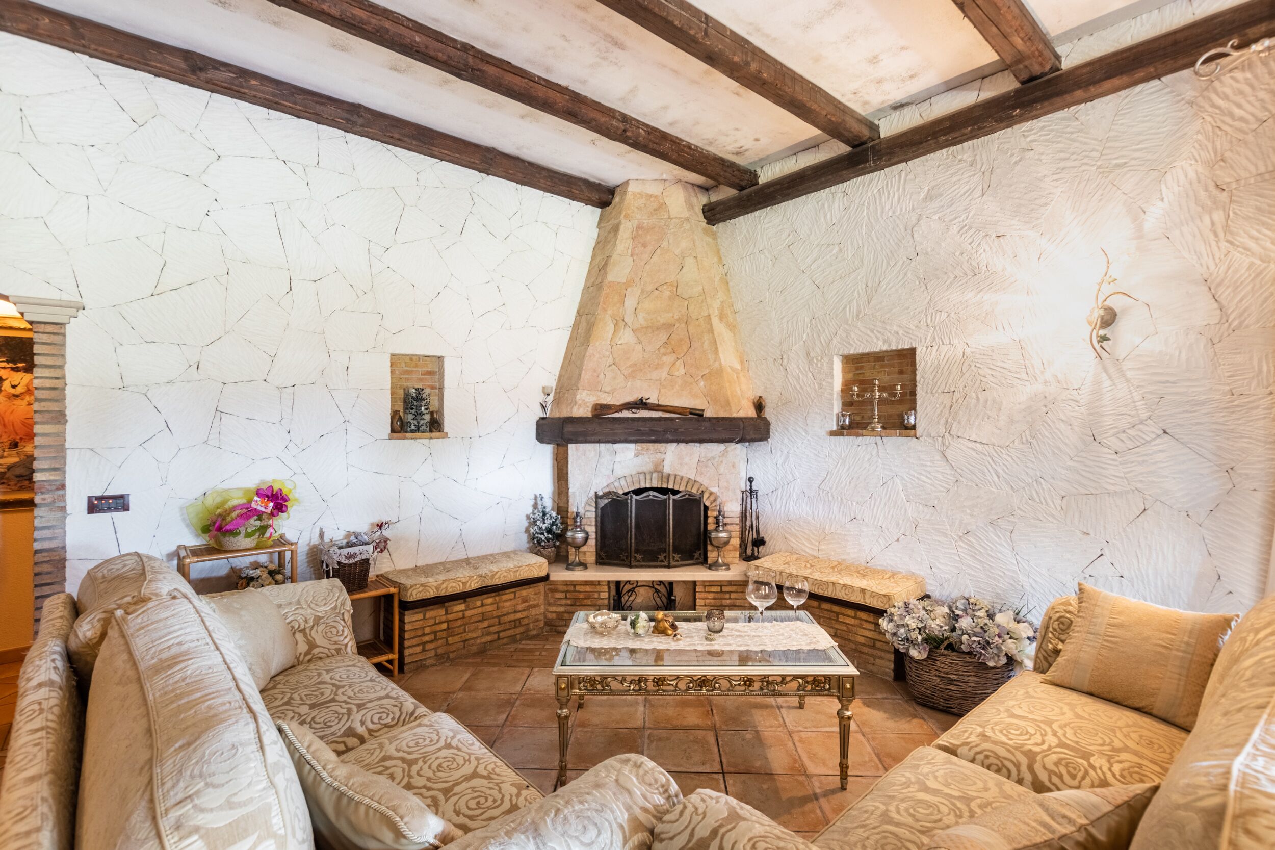 Una sala de estar acogedora con chimenea de piedra, sofás estampados y piso de baldosas.