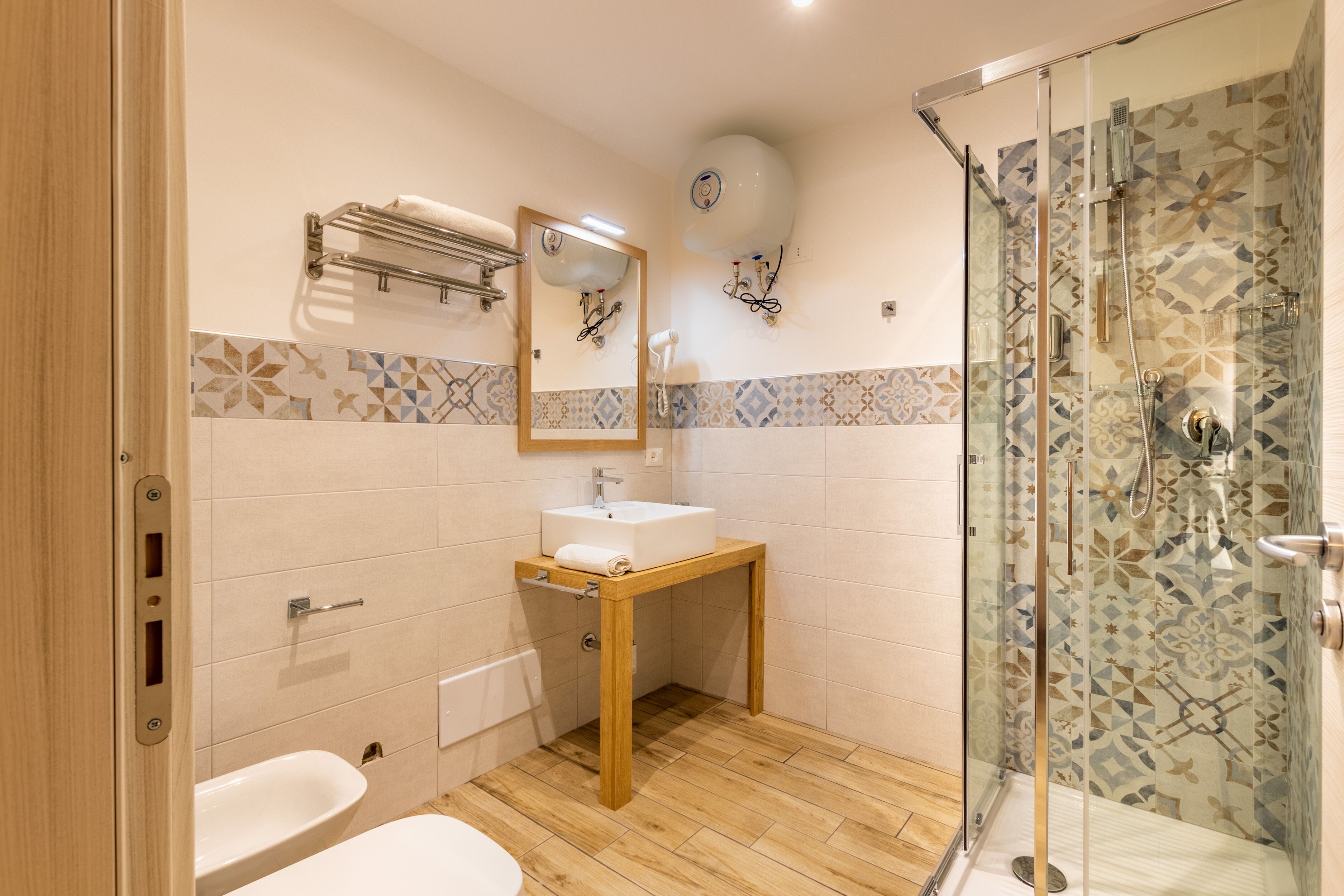 A bathroom with a wooden vanity, a glass shower enclosure, and patterned tiles.