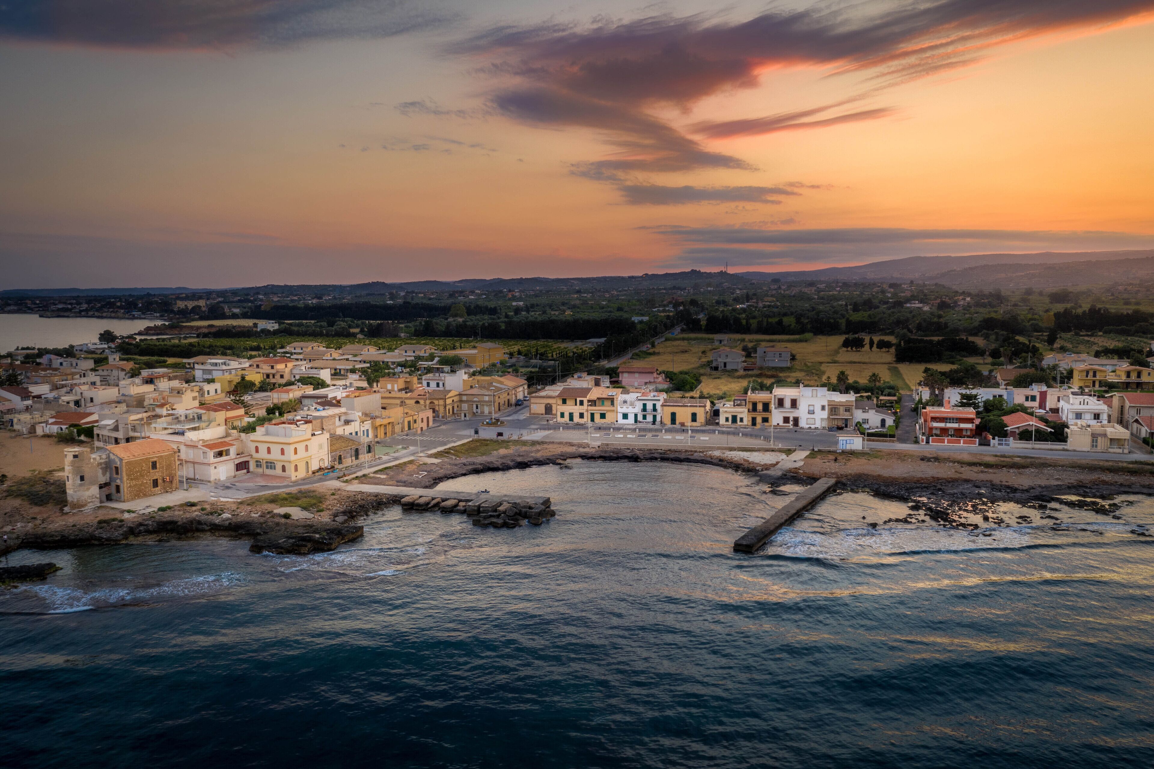 A coastal town with buildings along the waterfront, a clear sky, and a sunset.
