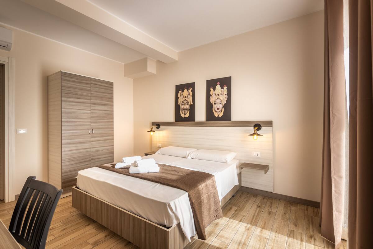 A hotel room with a bed, bedside tables, a wardrobe, and artwork on the wall.
